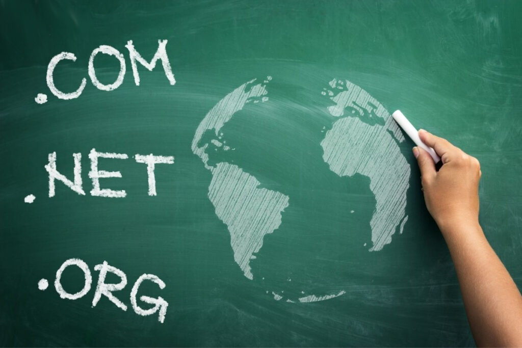 Ręka rysująca kredą kulę ziemską na tablicy obok popularnych rozszerzeń domen.
